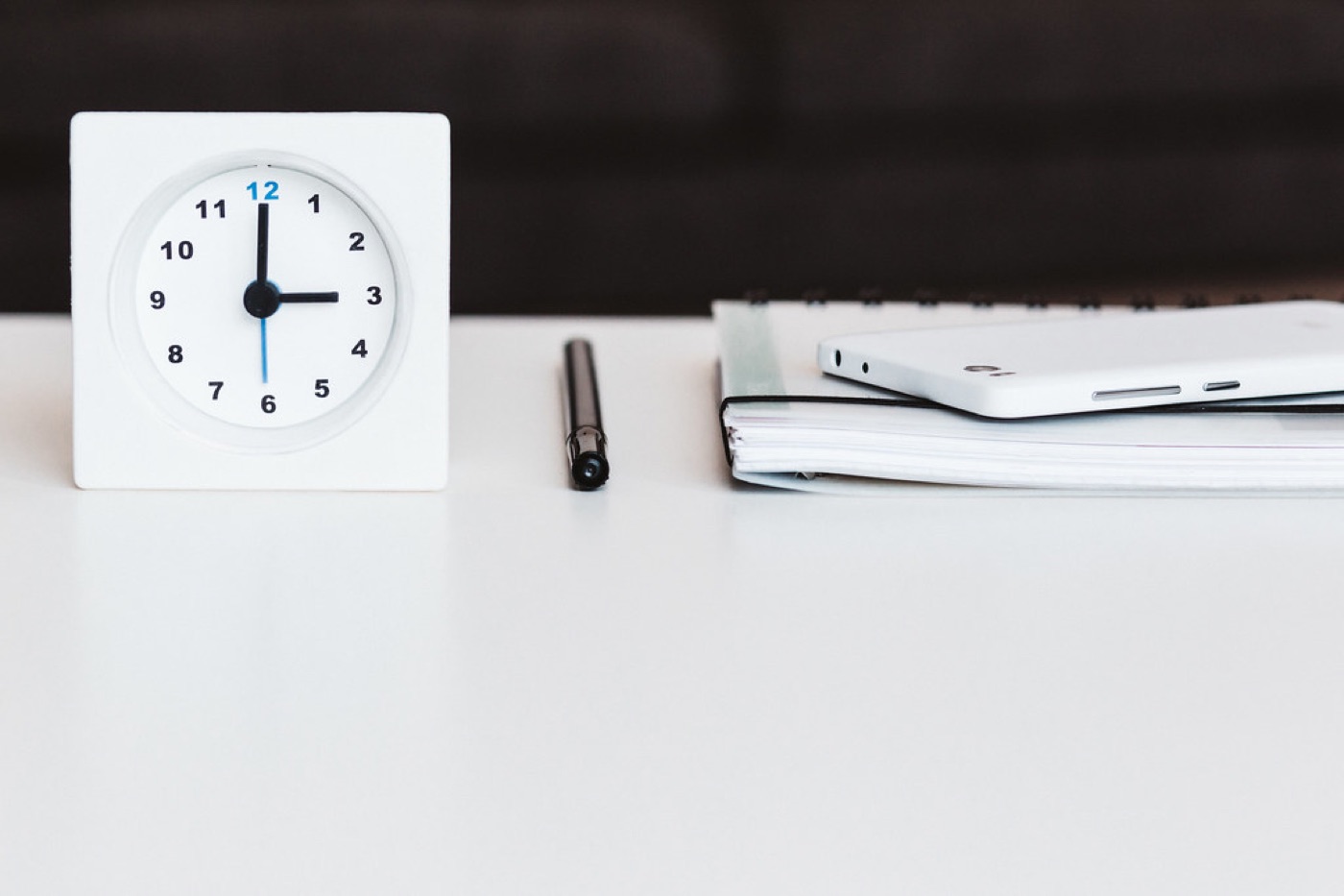 A paper calendar on a desk with three weeks marked off in pen beside a notebook and a candle.