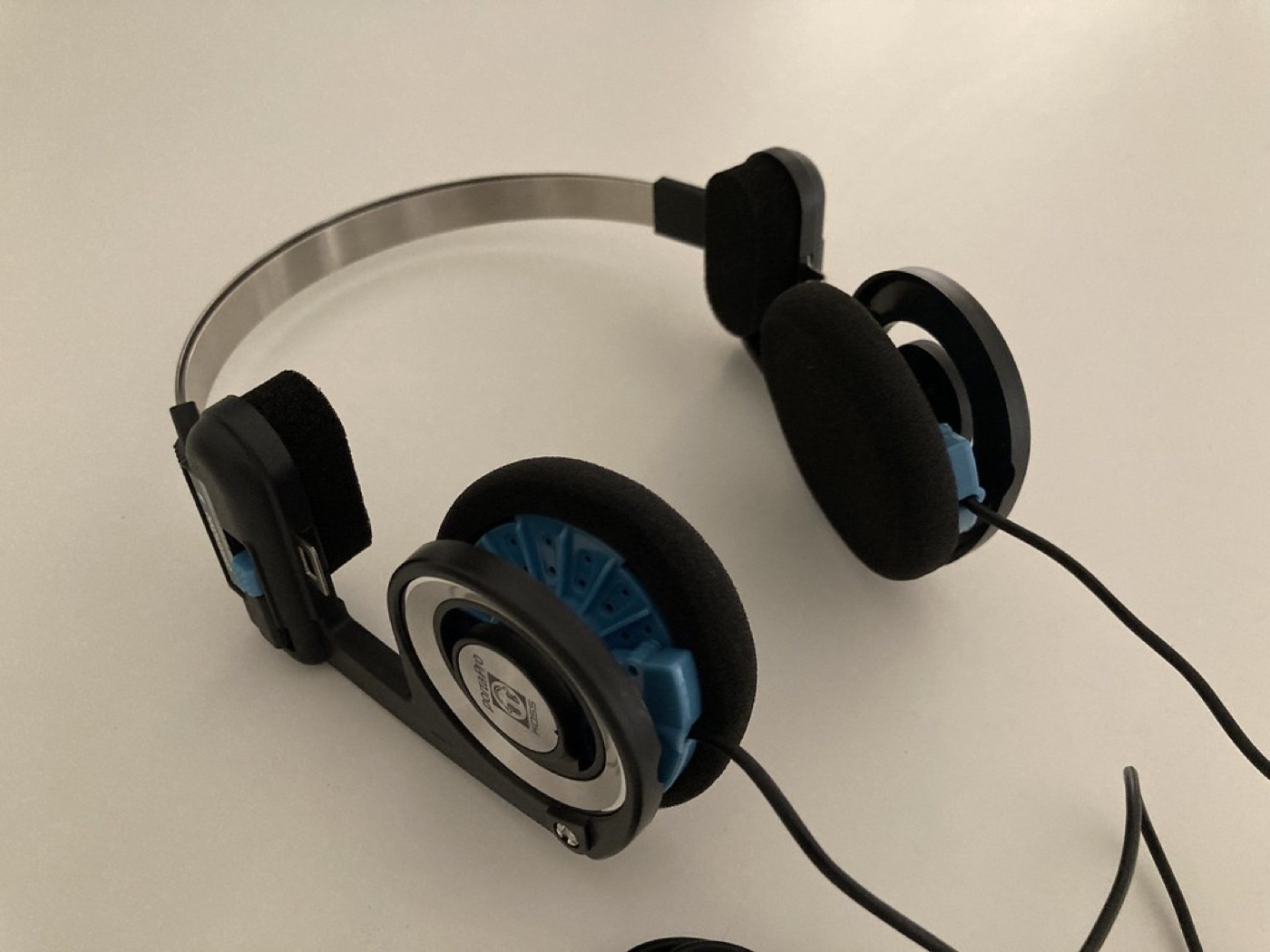 A pair of over-ear headphones rests on a dark desk beside a glowing lamp.