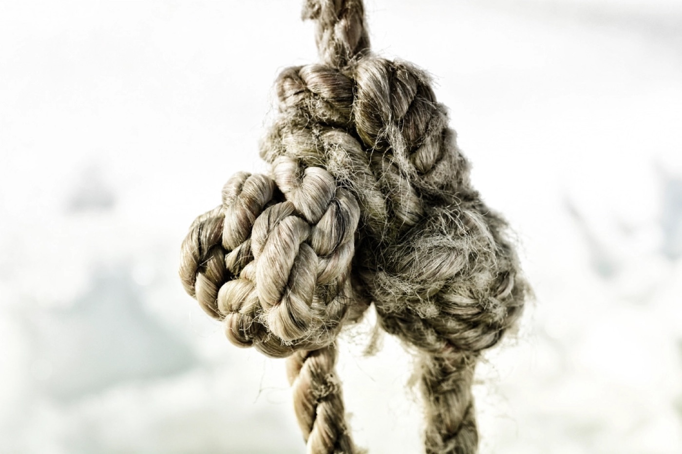 A tangled rope slowly being loosened by two hands on a wooden table.