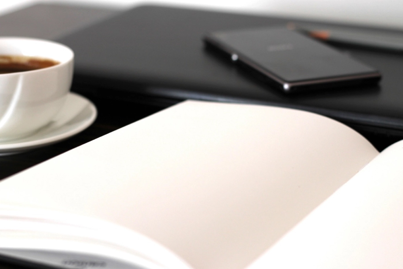 A cup of coffee and an open notebook on a table in soft morning light.